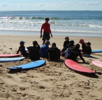 Teacher and students sitting on beach with surfboards
